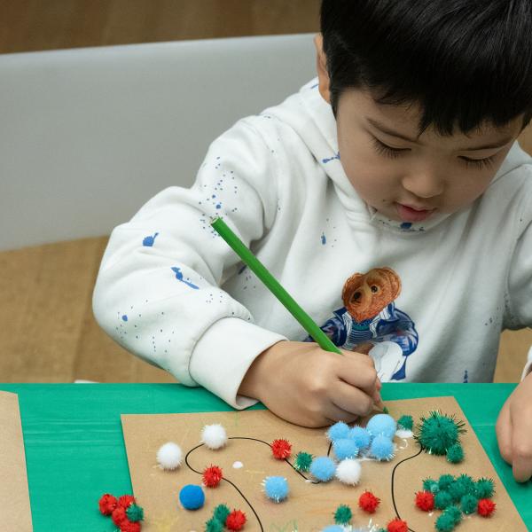 One child creating an artwork with colored pencils and collage.