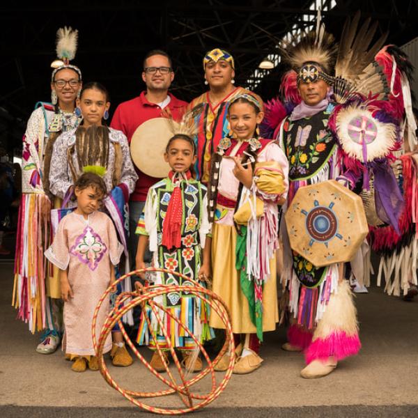 A group of adults and children in traditional clothing pose for a group photograph.