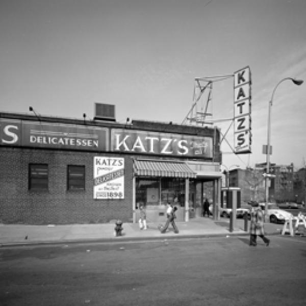 Vista exterior de Katz's Delicatessen en la intersección de las calles Ludlow y Houston con algunas personas caminando.