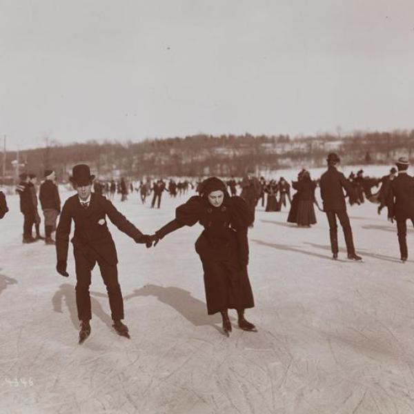 An outdoor museum photo of a man and women holding hands while ice skating with a group of people.