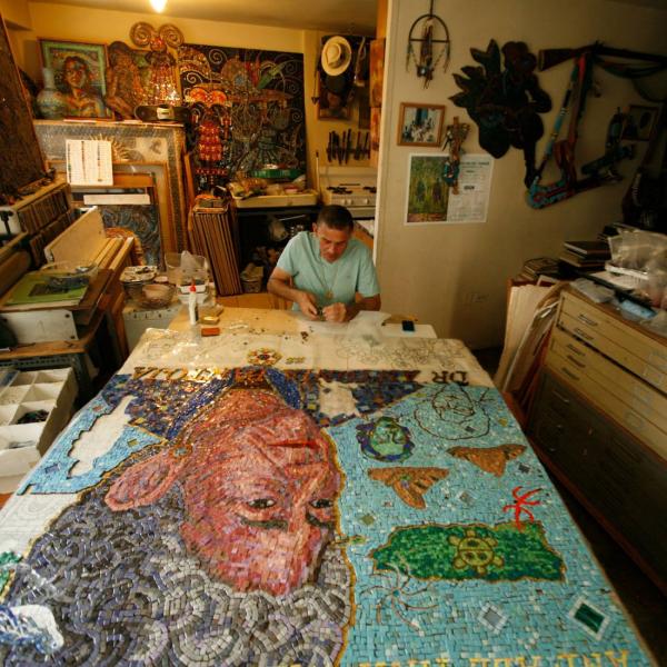 Manny works on a huge in progress mosaic on a table in his home studio.