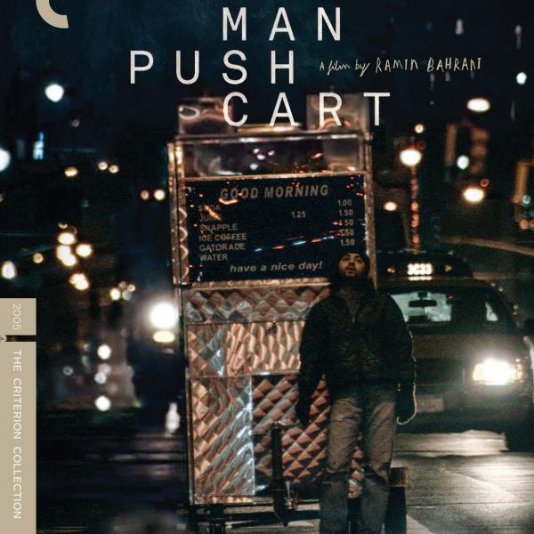A man pulling a push cart in the night. 