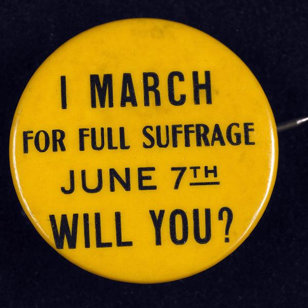 Um pequeno botão dourado apoiando os direitos de voto para mulheres do início do século 20 diz: I Marcha pelo Sufrágio Total, 7 de junho. Você poderia?