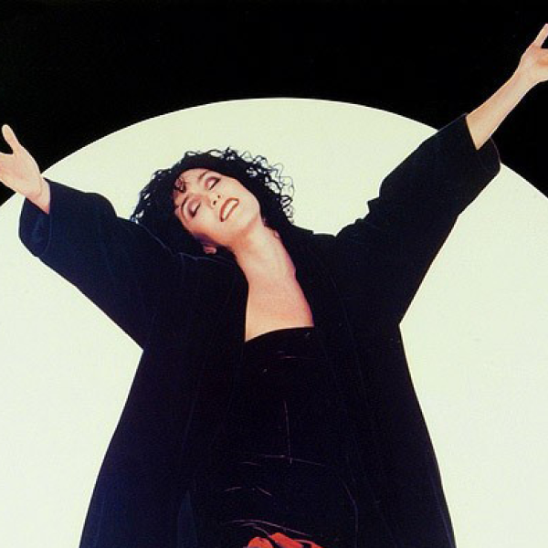 Cher holds her arms up in the air in front of a full moon. 