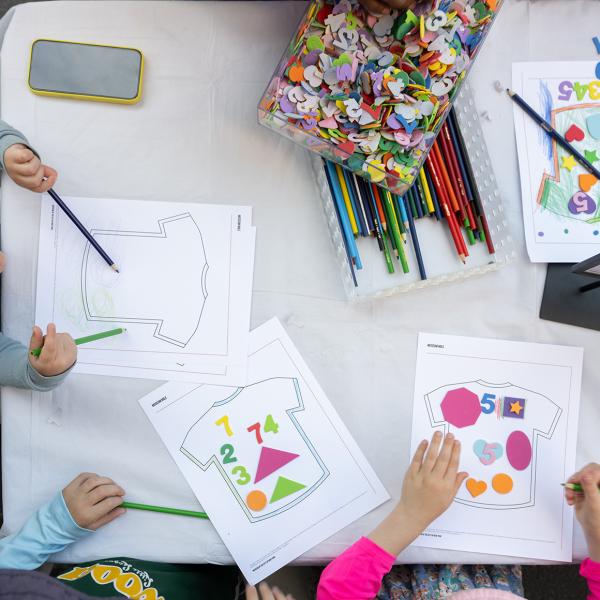 Three children creating an artwork with colored pencils and cut paper.