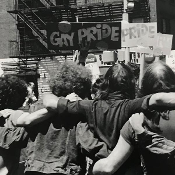 Photograph by Fred W. McDarrah of a group of people with their arms around each other and holding signs related to Pride
