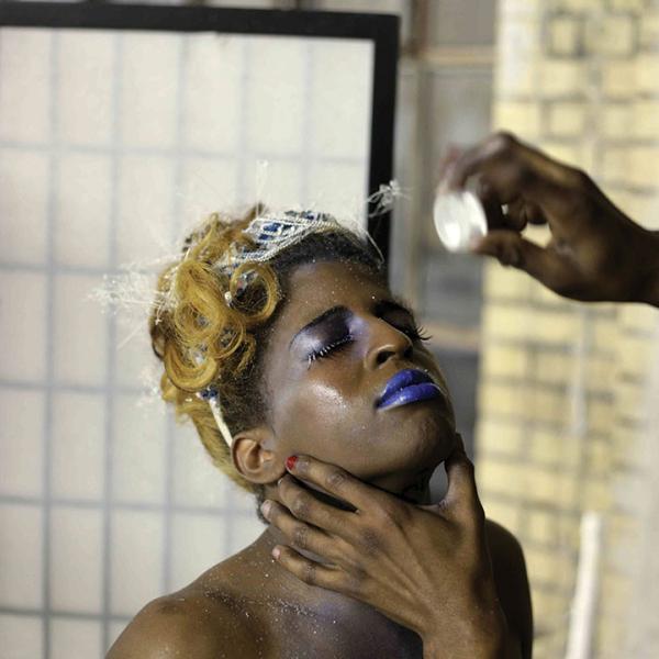 Krystal, une femme à la peau foncée, tient son visage vers le haut tandis qu'un bras lui tend la main et l'asperge de paillettes.