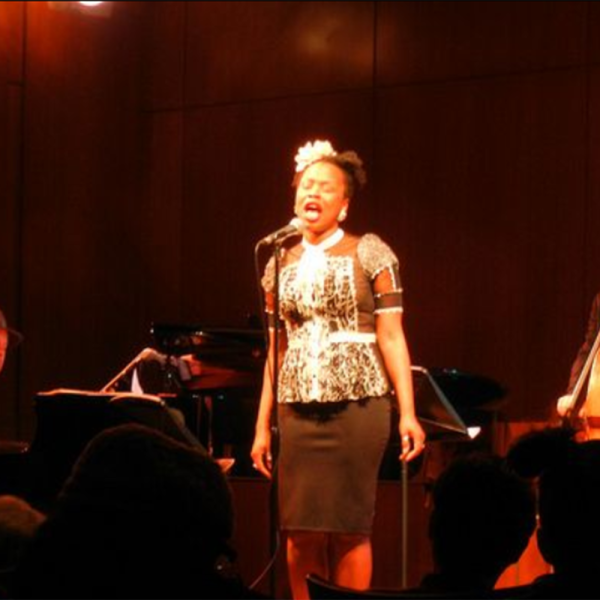 Image de la chanteuse reine esther chantant avec un groupe derrière elle devant un public en direct