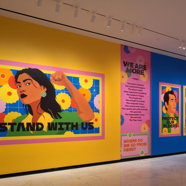 Installation shot of "Raise Your Voice," showing vibrant, colorful drawings of individuals with text.