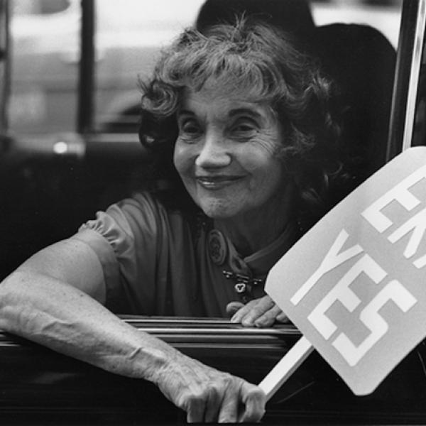 Alice Paul mira por la ventana de un vehículo con un cartel que dice "ERA SÍ"