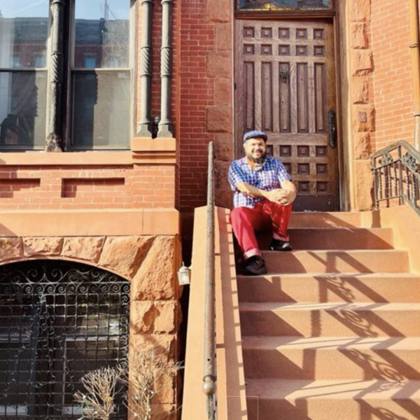 Monxo López sentado na escada em frente a uma casa de arenito