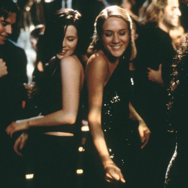 Kate Beckinsale and Chloë Sevigny smile and dance in black dresses in a crowded room. 