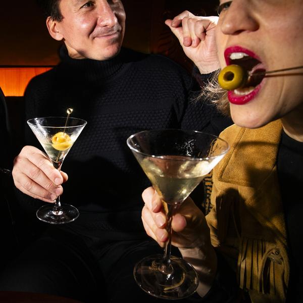 Two people drinking martinis with olives