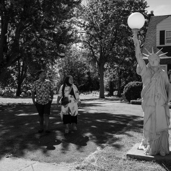 A man and a woman stand on a lawn next to a small replica of the Statue of Liberty.