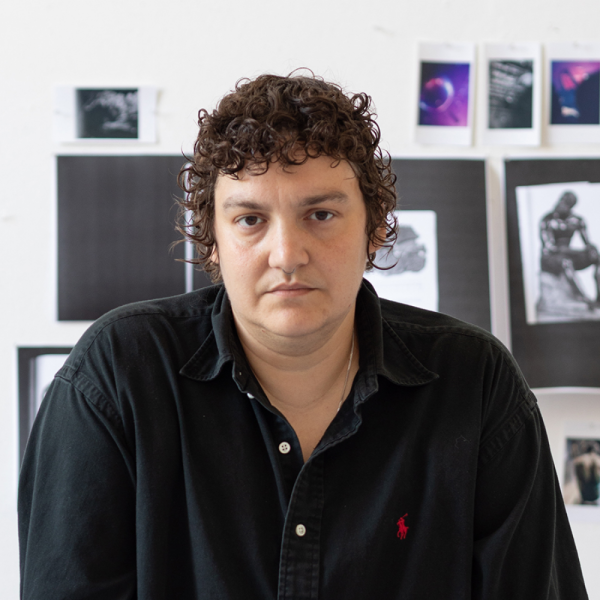 An artist in a black shirt smiling in front of their work