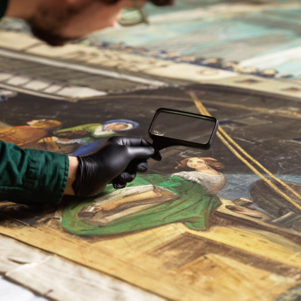 一名男子拿着放大镜仔细观察一幅画，画中画着一位身着绿色裙子的女人，旁边是一艘船。