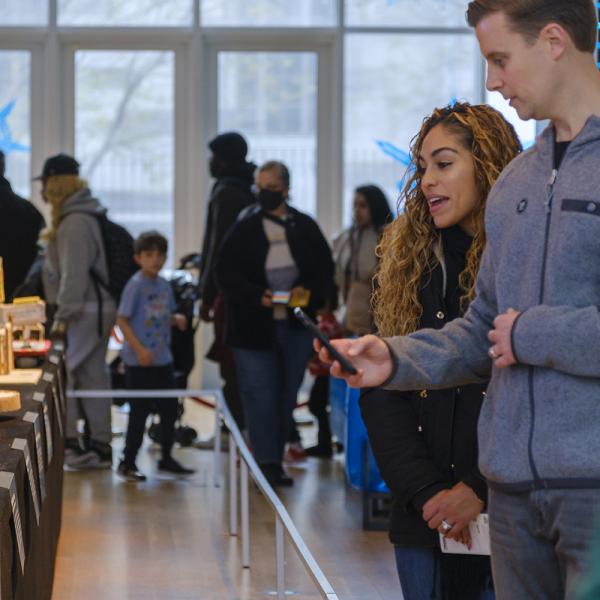Two people photographing and looking at a display made out of gingerbread with a crowd in the background.
