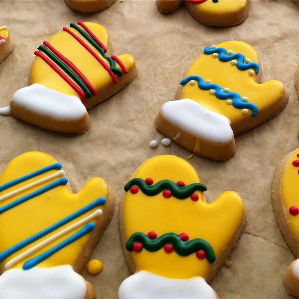 Mitten-shaped cookies decorated with yellow, red, blue, green and white icing in various patterns.