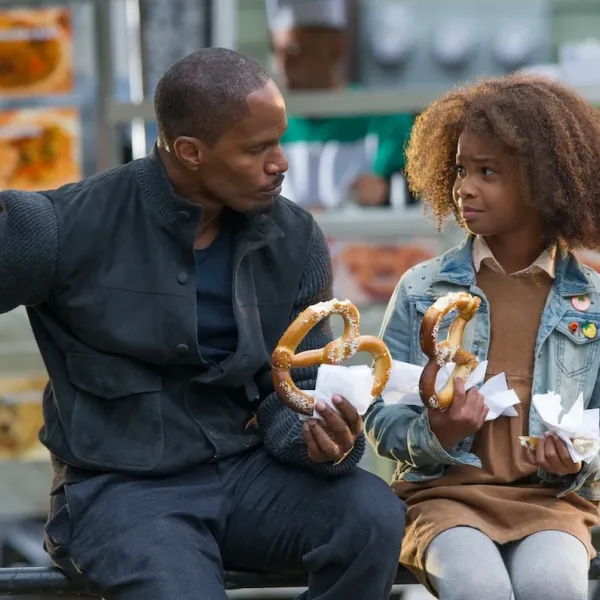 A man and young girl sitting in public eating pretzels in front of New York City street food cart.
