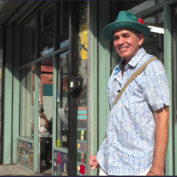 A man standing in Spanish Harlem in NYC smiling with a green hat