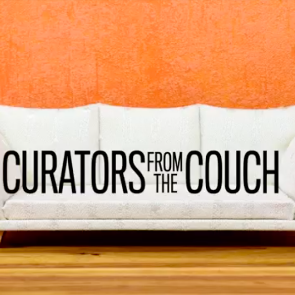 White couch against an orange painted wall and wood floor. Text on the couch reads "Curators from the Couch" in black letters.