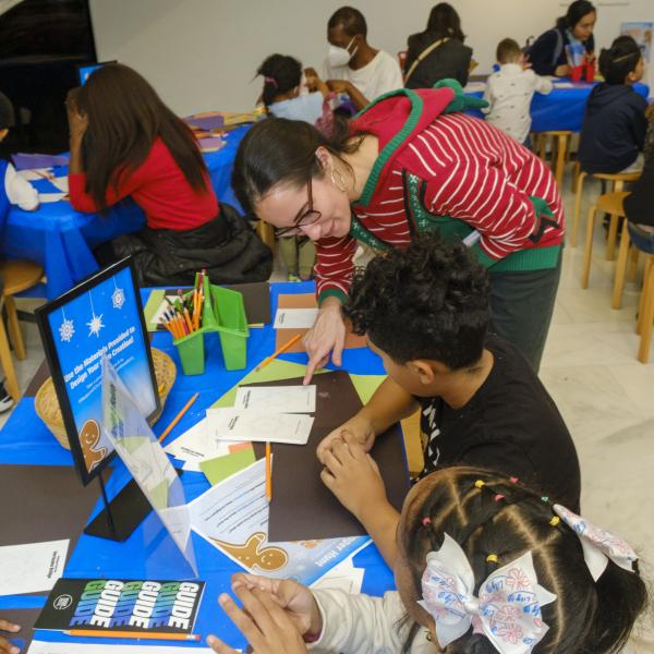 A woman helps a young child with an art project at a table. 