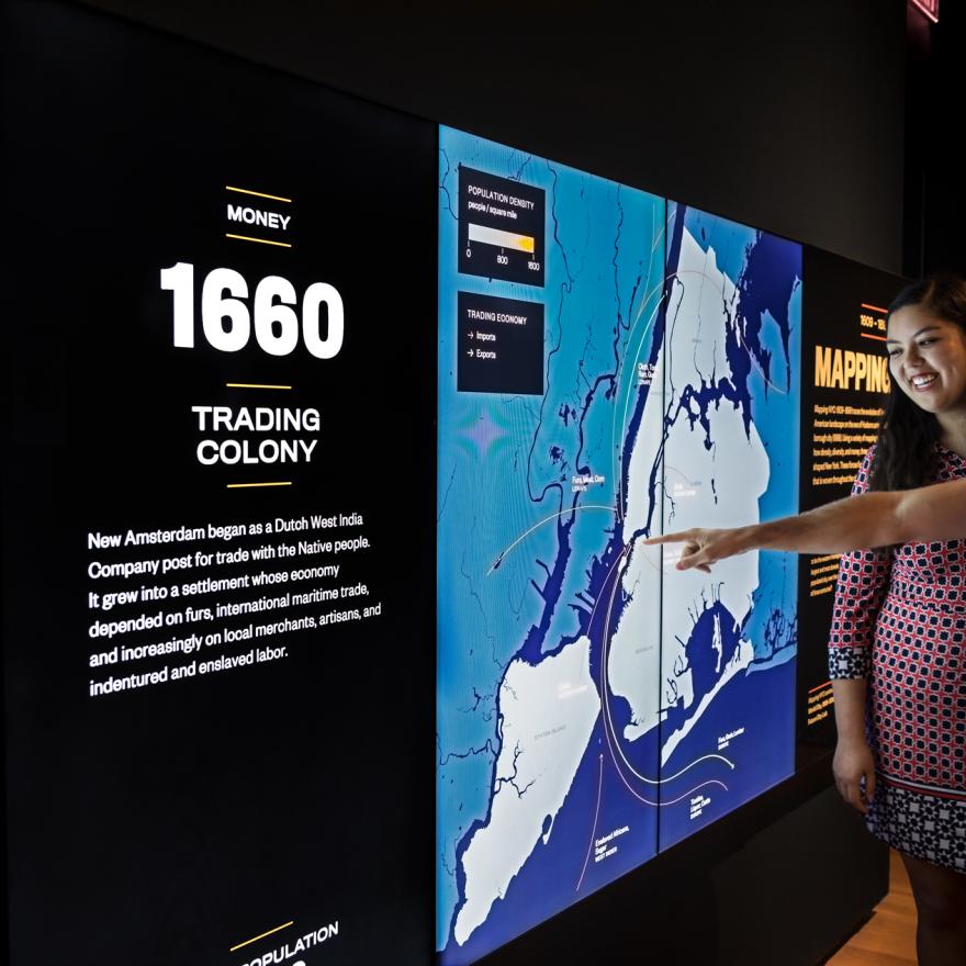 Two visitors point out details on a screen in an exhibition space