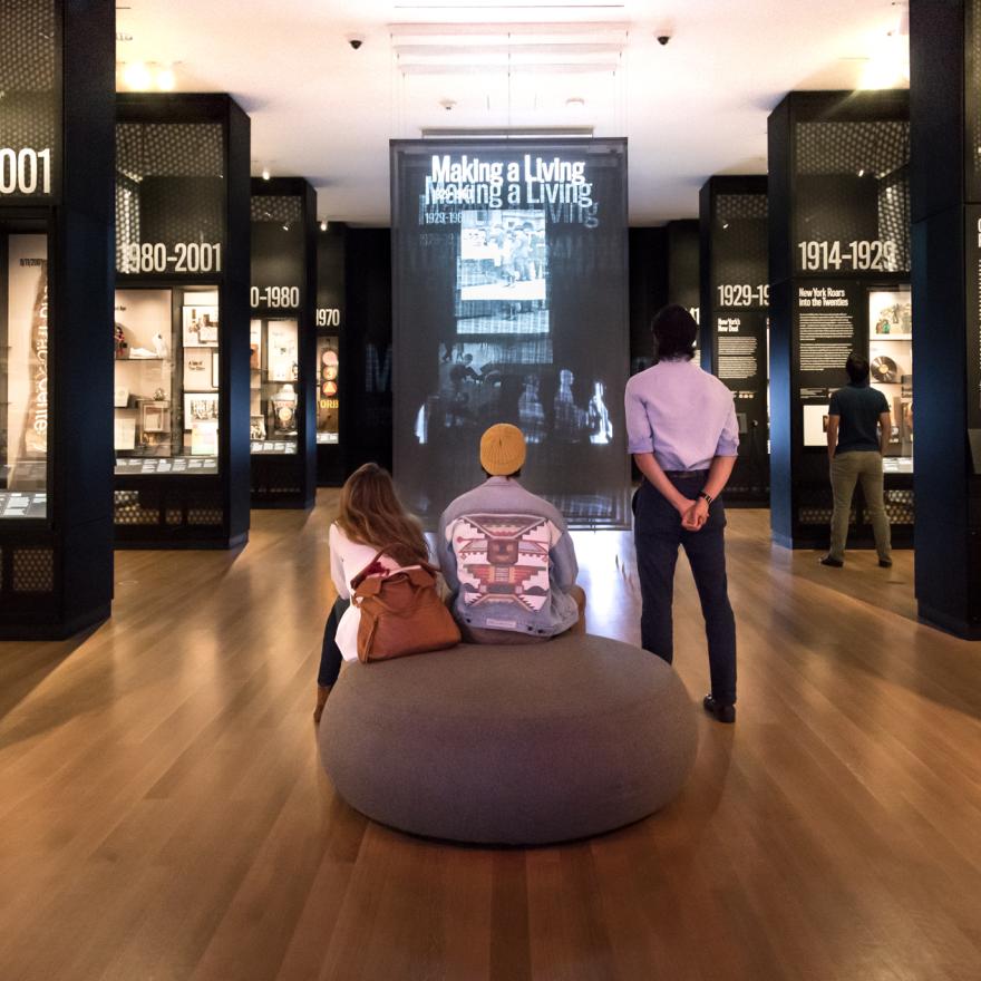 Visitors sit and stand while looking at a video display in a gallery