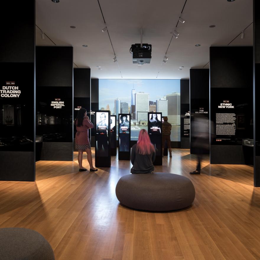 Visitors sit and stand around an exhibition at the Museum of the City of New York