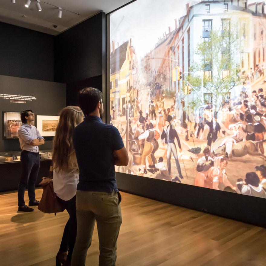 Os visitantes olham para uma grande projeção em um espaço de exposição