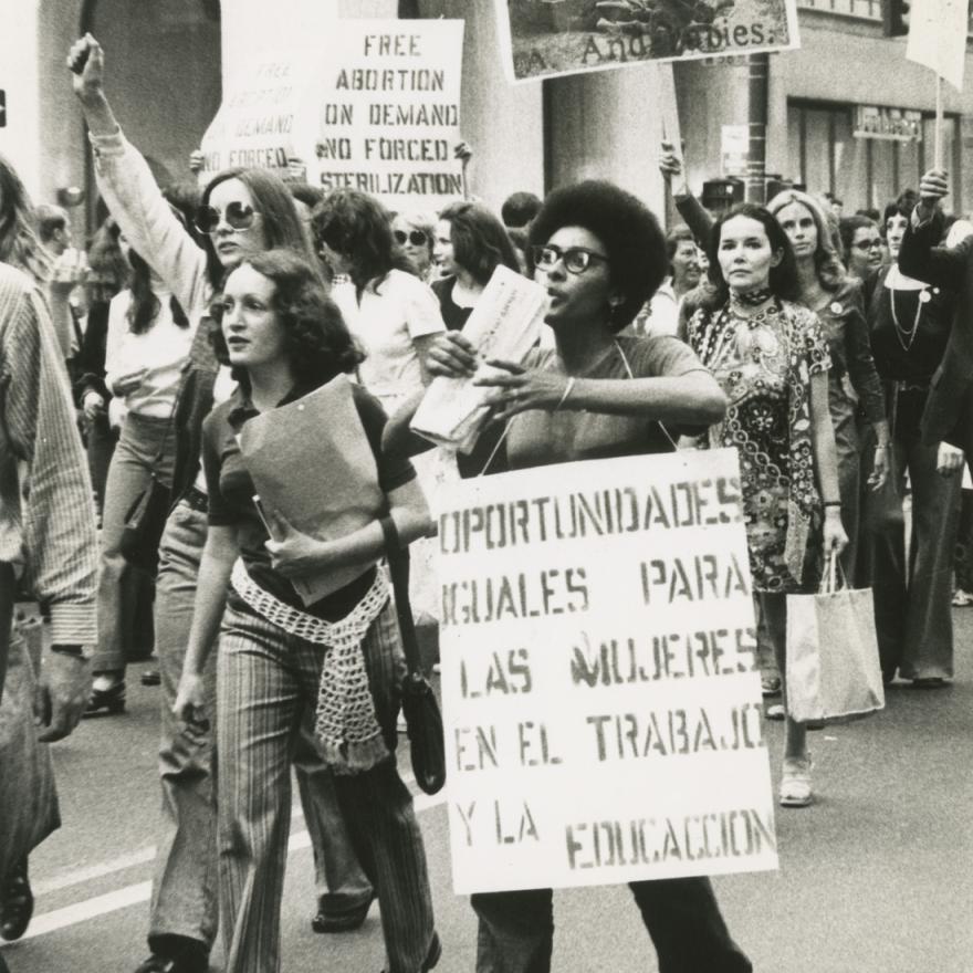 A group of women march in a rally, many are holding protest signs