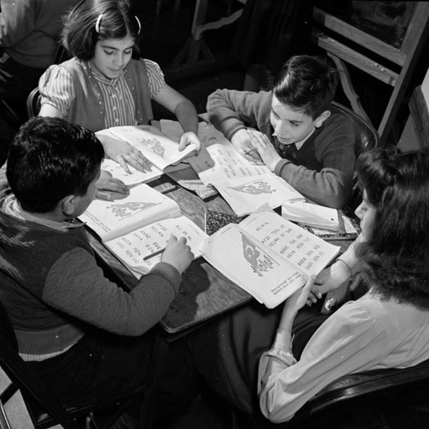 Quatro crianças sentam-se ao redor de uma mesa olhando os livros na frente deles