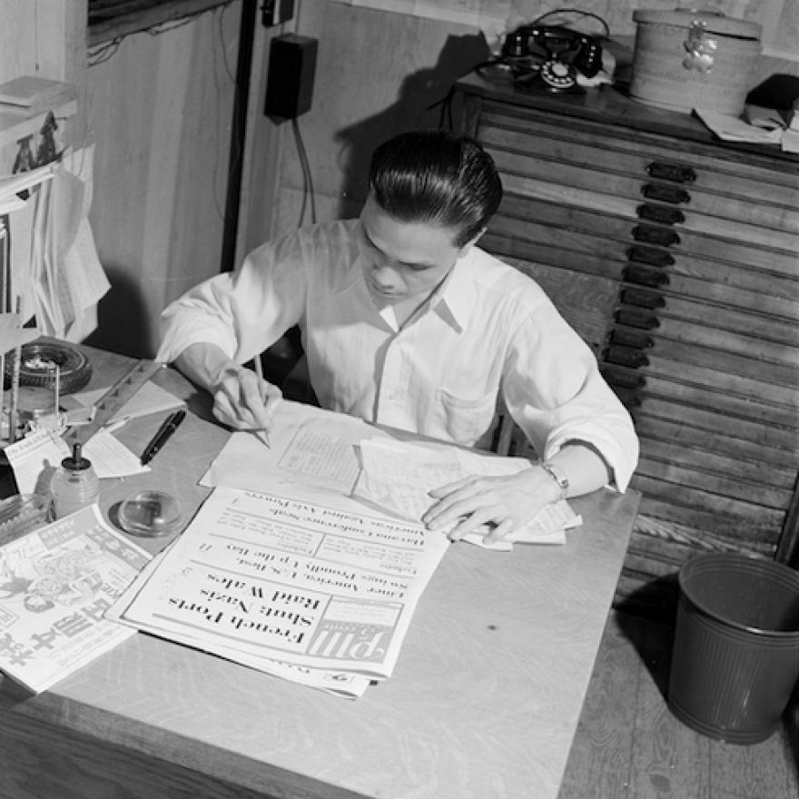 Photographie d'un homme assis à une table entouré de journaux