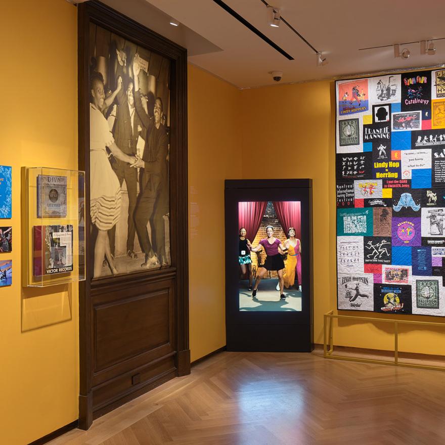 Installation of Urban Stomp with large artworks and an interactive screen in a room with yellow walls