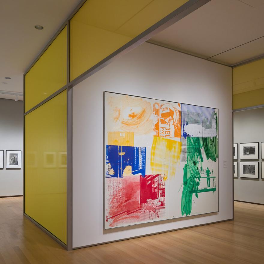 Installation of Robert Rauschenberg’s New York with a large artwork in front of a wall of photographs
