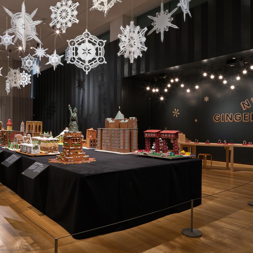 A long table with gingerbread houses inspired by New York, with lights and snowflakes hanging above