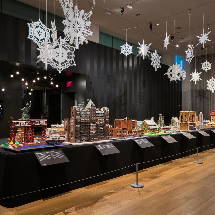 A long table with gingerbread houses inspired by New York, with lights and snowflakes hanging above