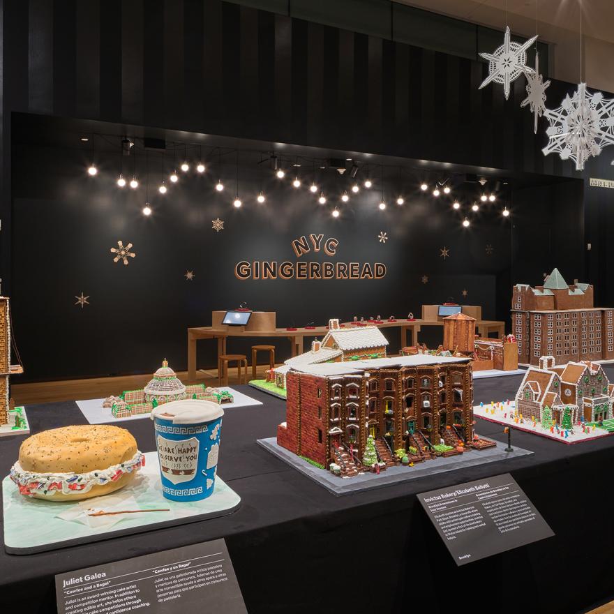 A long table with gingerbread houses inspired by New York, with lights and snowflakes hanging above