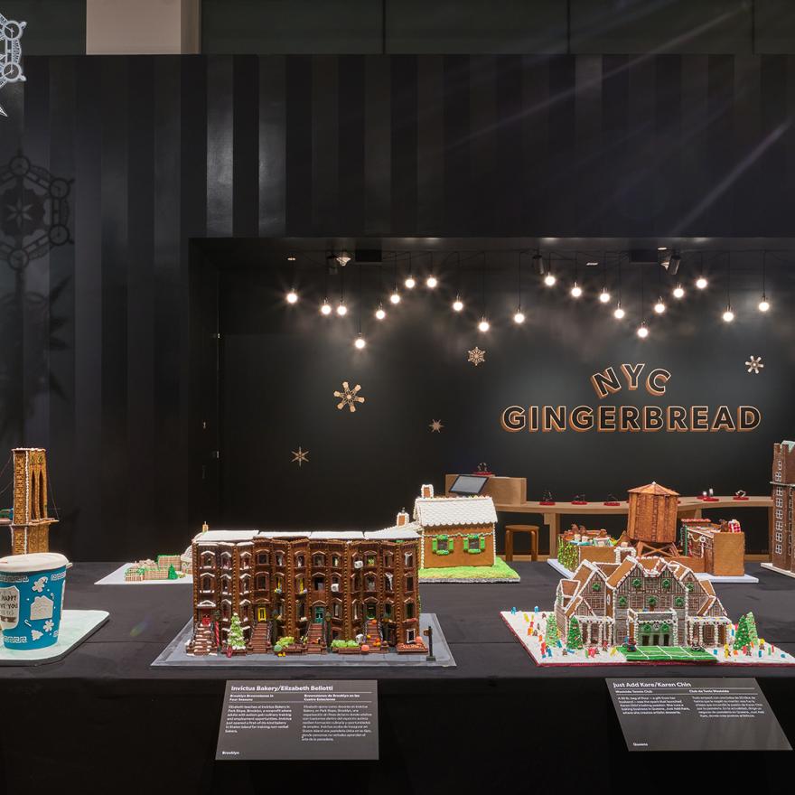 A long table with gingerbread houses inspired by New York, with lights and snowflakes hanging above