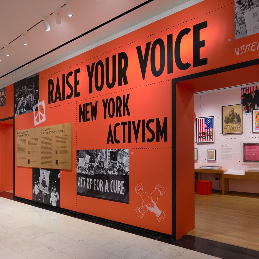 A gallery wall painted bright red and reading Raise Your Voice: New York Activism