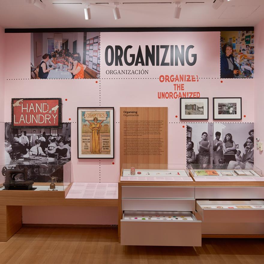 A gallery with pink walls and wooden cases showing photographs, sculptures, paintings, and interactive displays