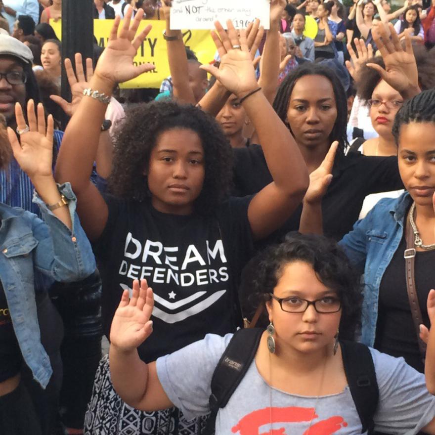 Manifestantes da Black Lives Matter com as mãos no ar em sinal de rendição e o slogan "mãos para cima não atiram"