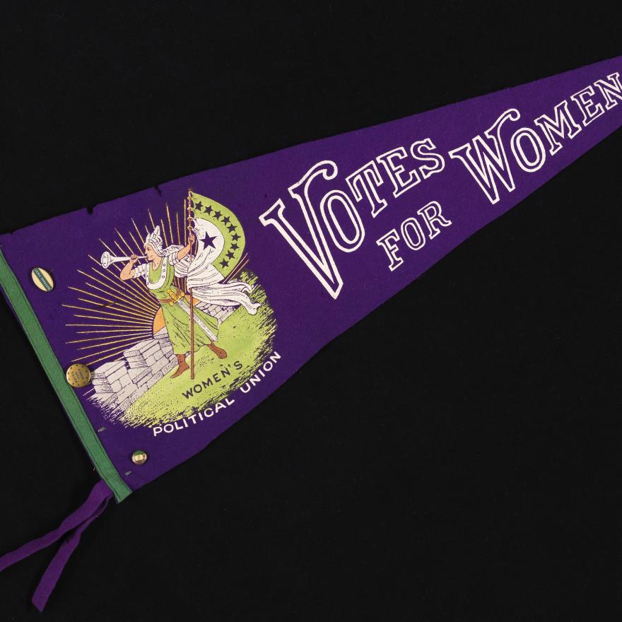 Pendentif violet avec "Votes pour les femmes" en texte blanc, et un dessin d'une femme viking-eqsue soufflant une trompette