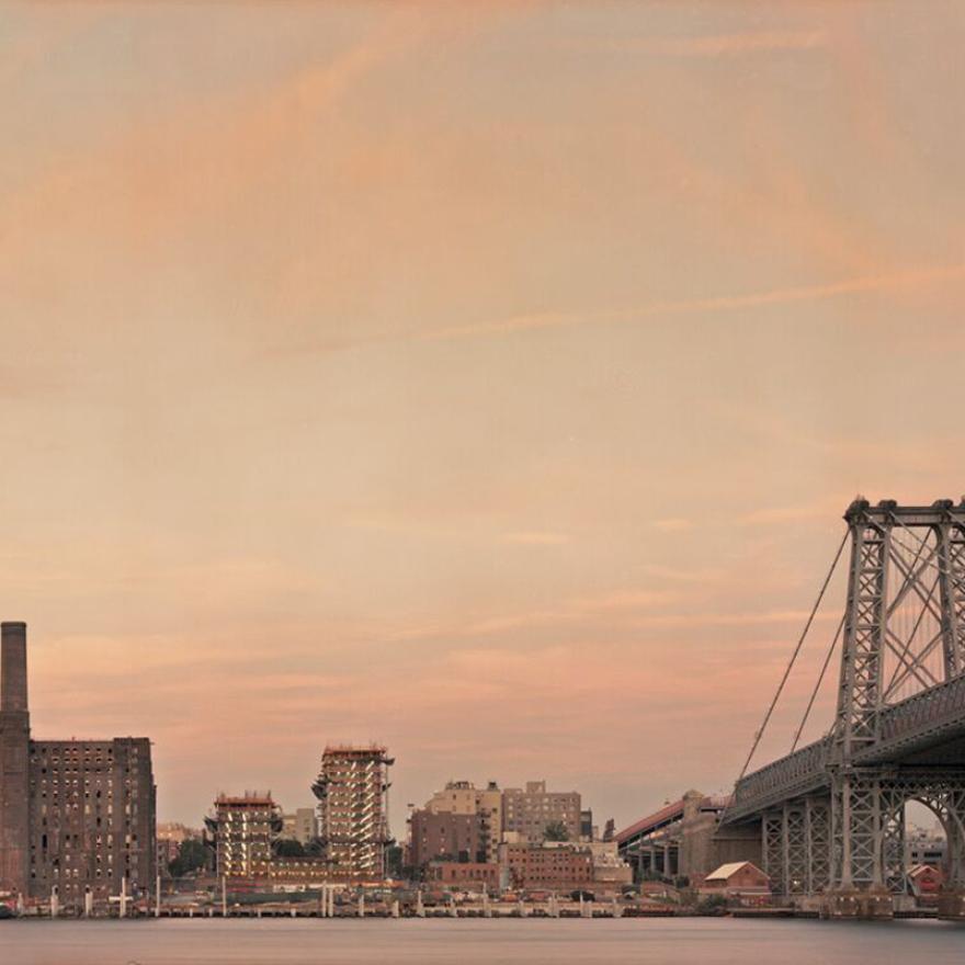 bridge and series of buildings on the waterfront are lit by an orange-purple sunset