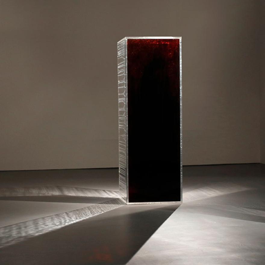 Rectangular prism that is reflective on two sides, and blood-red on the side facing the camera. Light is reflecting off it