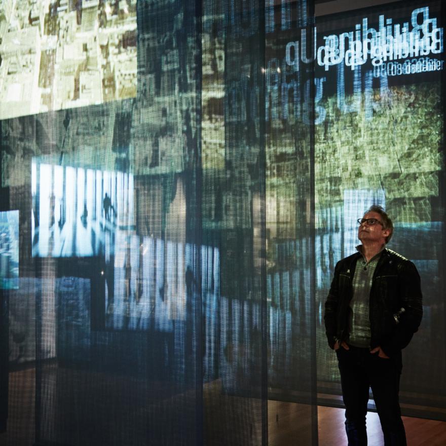 A visitor stands in-between sheer panels as a video projection plays across them