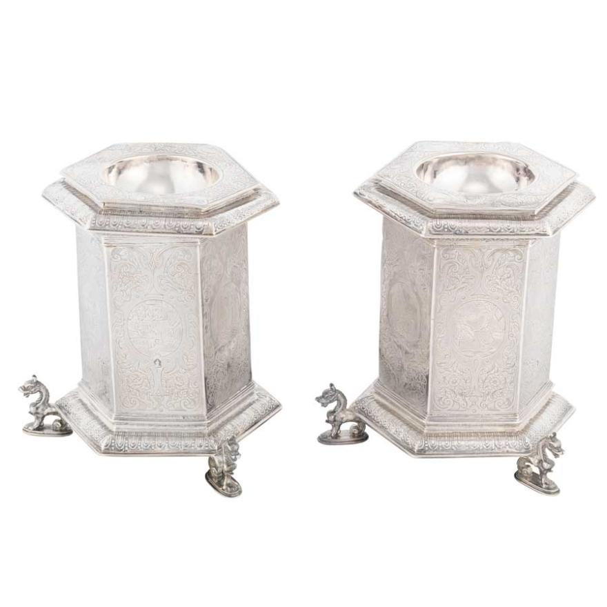 Two intricately detailed silver containers shaped like a hexagonal prism, with an indent at the top to hold salt