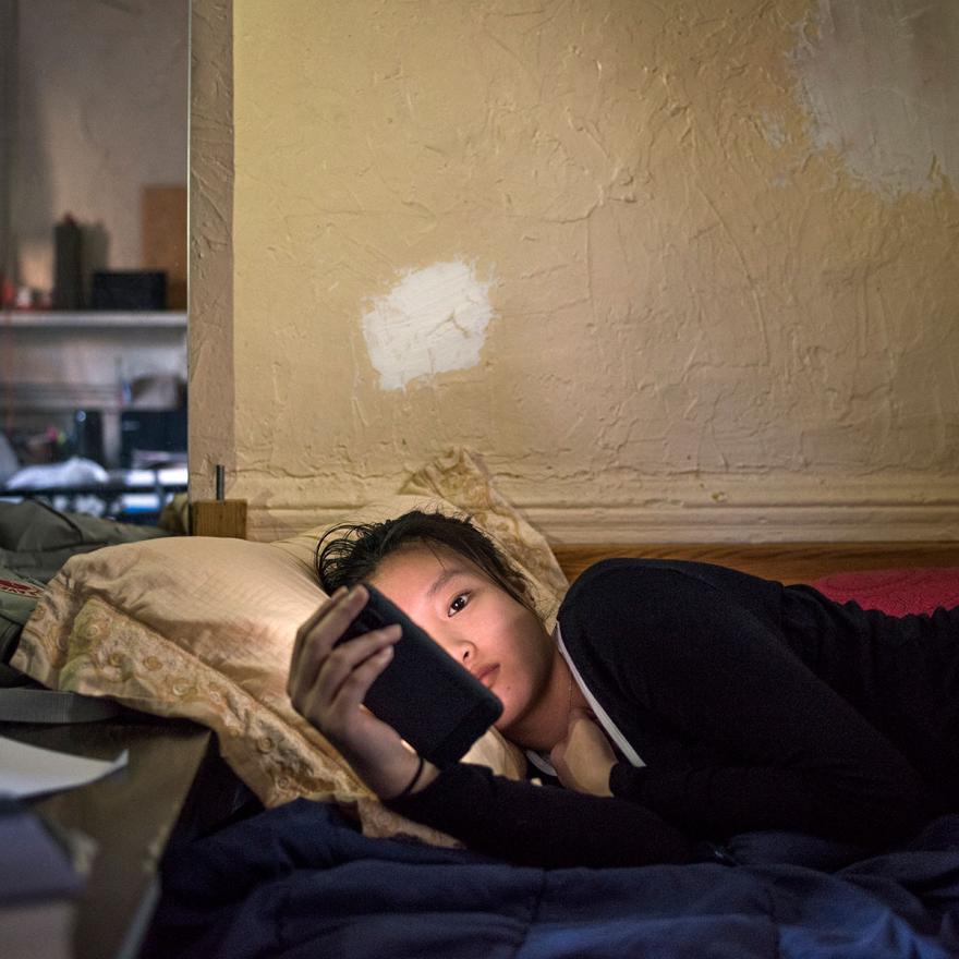 Una joven china yace en una cama o sofá mirando su teléfono.
