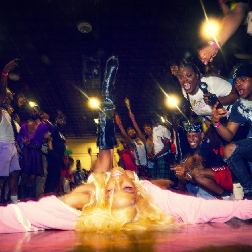 Woman in wearing pink dancing on the floor surrounded by an energetic crowd of people