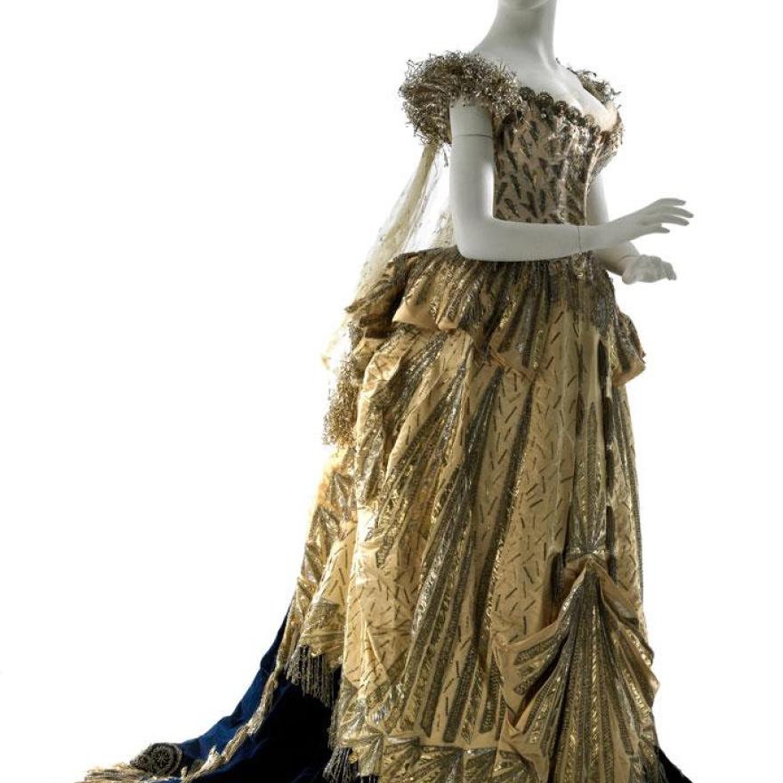 A gold floor-length dress with metallic details, a black underskirt, and blue train